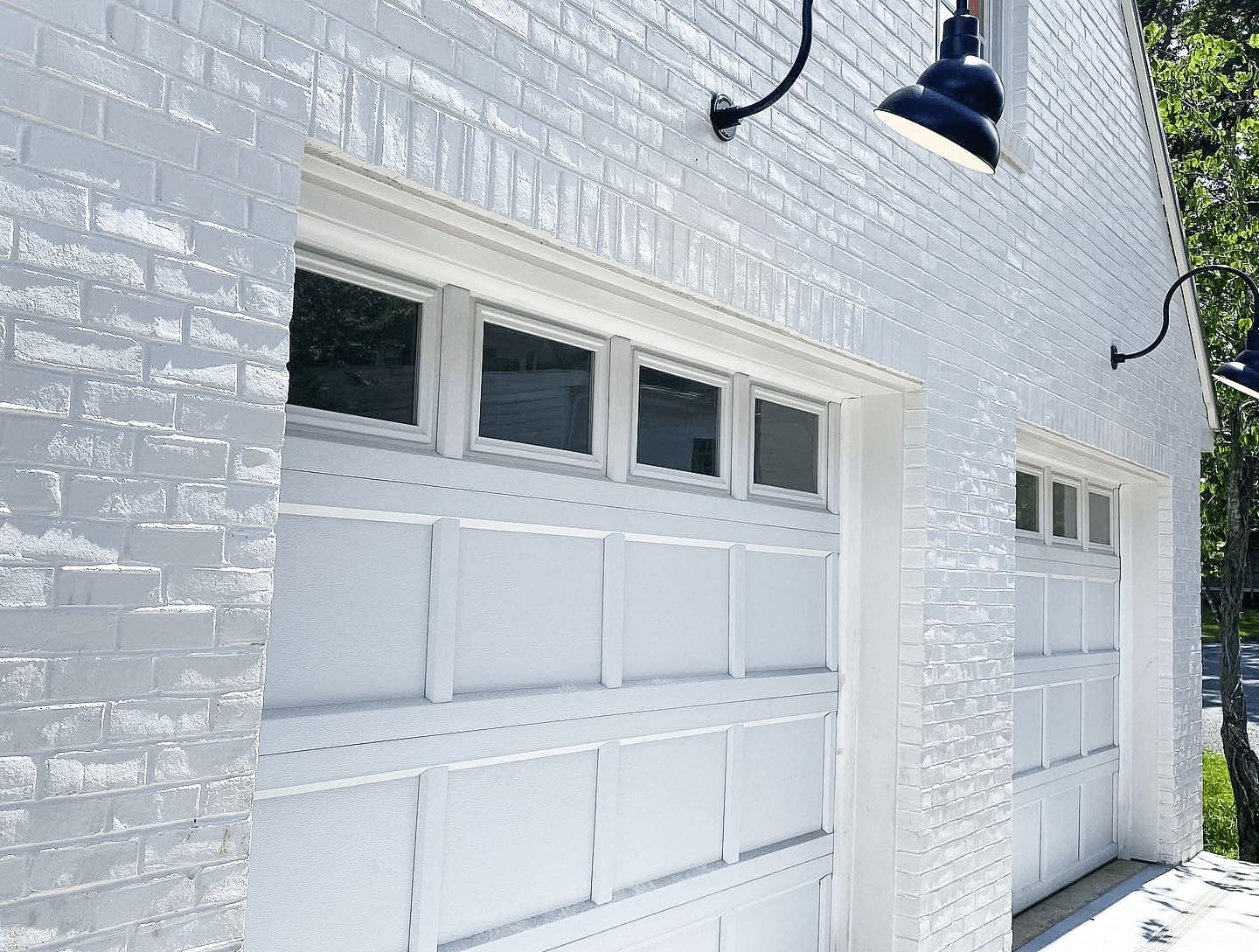 White brick garage facade with two paneled garage doors and small rectangular windows above, lit by outdoor black lamps.